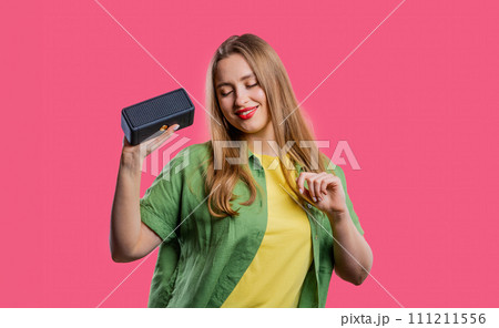 Young woman listening to music by wireless portable speaker - sound system pink Young woman listening to music by wireless portable speaker - sound system pink 111211556
