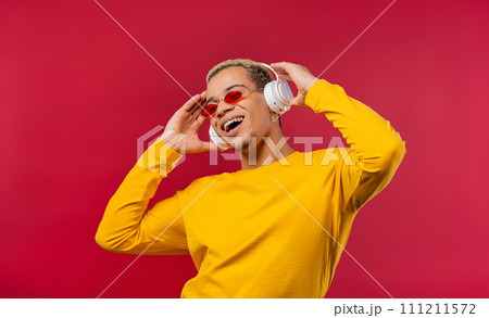 Positive man listening music, enjoying dance with headphones on red studio Positive man listening music, enjoying dance with headphones on red studio 111211572