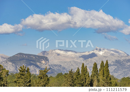 Majestic Mountain Range Overlooking a Lush Green Forest Under a Cloud-Filled Sky Majestic Mountain Range Overlooking a Lush Green Forest Under a Cloud-Filled Sky 111211579