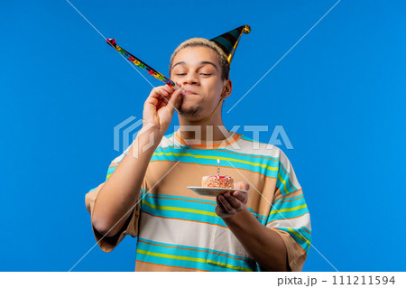 Happy birthday man making wish - blowing candle on cake. Curly haired guy 111211594