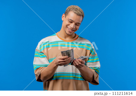 Satisfied man counting USD currency. Young millenial guy or student counts money Satisfied man counting USD currency. Young millenial guy or student counts money 111211614