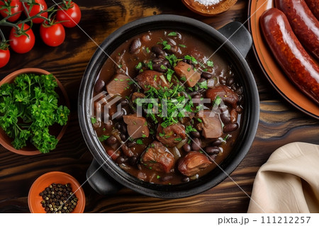 Top view of traditional Brazilian dish feijoada in black clay bowl on a wooden table 111212257