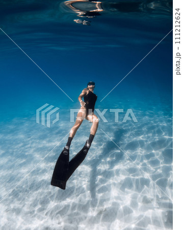 Freediver swimming underwater in tropical sea over sandy bottom. Female swims with fins undersea Freediver swimming underwater in tropical sea over sandy bottom. Female swims with fins undersea 111212624