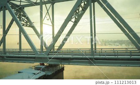 Volkhov, Russia, the railway bridge over the Volkhov River next to the hydroelectric power station. Severe frost -30 degrees Celsius. Low polar sun. Yellow cold fog. 111213013