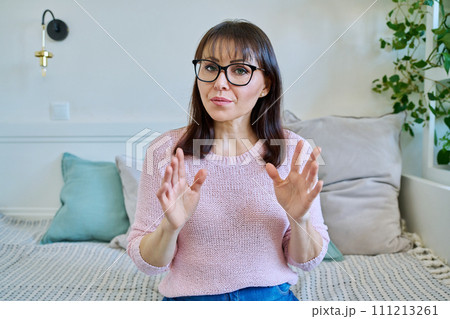 Webcam view of middle-aged woman talking, sitting on couch at home 111213261