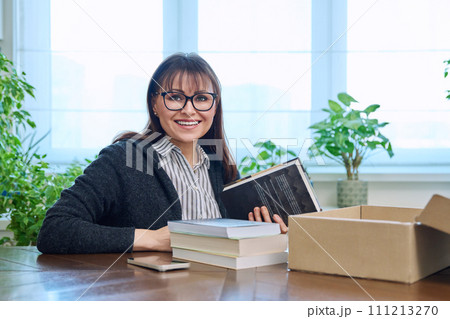 Middle-aged joyful woman with new books unpacked from cardboard box Middle-aged joyful woman with new books unpacked from cardboard box 111213270