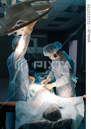 Vertical shot of being operated by professional surgeons. Male doctor adjusting light performing operation wearing medical gown. Surgeon adjusting surgical lamp before operation. Concept of emergency. Vertical shot of being operated by professional surgeons. Male doctor adjusting light performing operation wearing medical gown. Surgeon adjusting surgical lamp before operation. Concept of emergency. 111213719