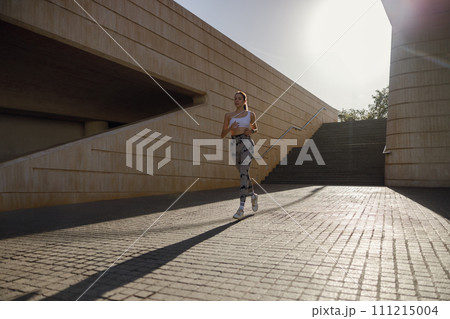 Active woman athlete is jogging on morning on modern building background. Healthy life concept Active woman athlete is jogging on morning on modern building background. Healthy life concept 111215004