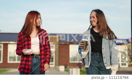Two happy female teenager friends walking talking smiling together takeaway fast food coffee weekend 111218766