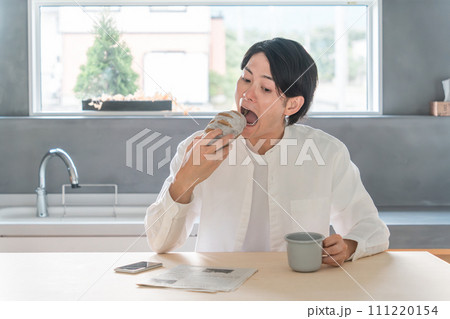 家で新聞を読みながら朝食・パンを食べる若いアジア人男性 111220154