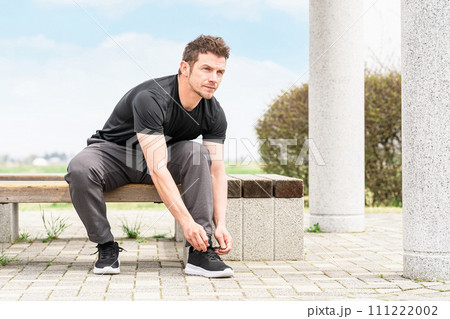 スニーカーの靴紐を結んで運動の準備をするスポーツウェアを着た白人男性 111222002