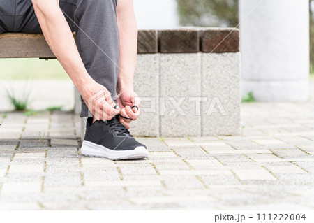 スニーカーの靴紐を結んで運動の準備をするスポーツウェアを着た白人男性 111222004
