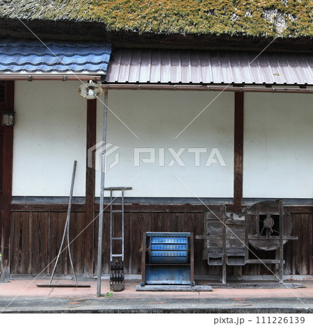 茅葺の古い木造建築の白壁と昔の農機具 茅葺の古い木造建築の白壁と昔の農機具 111226139