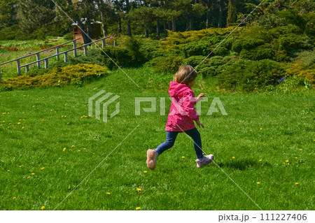Adorable child in a red jacket runs through a green meadow 111227406