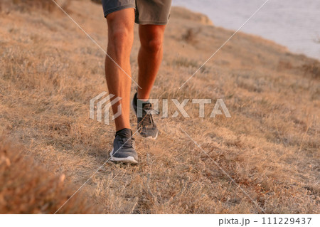 Legs of sporty man walking outdoor with warm sunset. 111229437