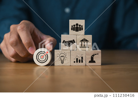 Hand stacking wooden blocks of business icons representing key elements of business success including target, teamwork, partnership, innovation, and growth. Hand stacking wooden blocks of business icons representing key elements of business success including target, teamwork, partnership, innovation, and growth. 111230416