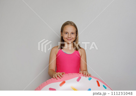 Cheerful child girl with pink rubber inflatable ring swimming pool float standing  111231048
