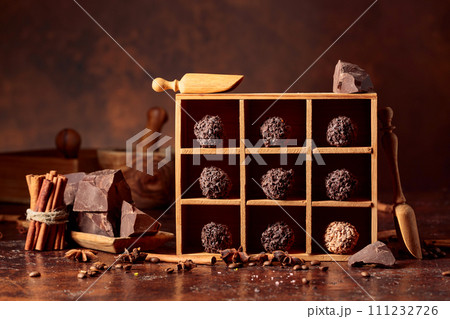 Chocolate candy in wooden box, broken pieces of chocolate, cinnamon sticks, anise and coffee beans. 111232726