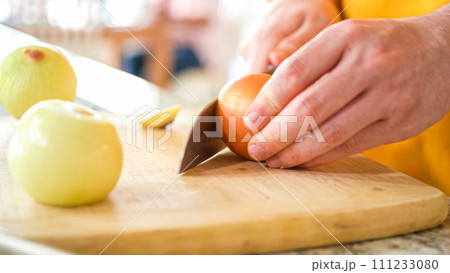 In the welcoming setting of a modern kitchen, a young man continues his dinner preparation process. He's currently involved in slicing yellow onions into rings, prepping them for grilling on an In the welcoming setting of a modern kitchen, a young man continues his dinner preparation process. He's currently involved in slicing yellow onions into rings, prepping them for grilling on an 111233080