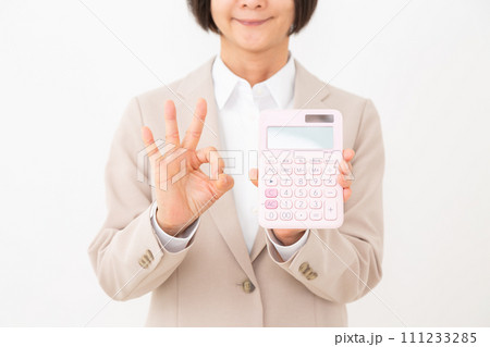 ピンク色の電卓を持って指で丸サインをするベージュのスーツを着たミドル女性のビジネスウーマン 111233285
