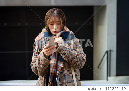 スマホを持つマフラーを巻いた冬服の若い女性 111235130