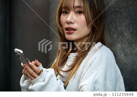 壁に寄りかかってスマホを操作する若い女性 壁に寄りかかってスマホを操作する若い女性 111235648