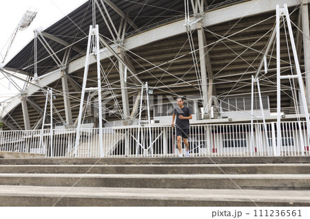 Young athlete asian man running in front of the stadium. The man trains outdoors. Preparing for the marathon. Young athlete asian man running in front of the stadium. The man trains outdoors. Preparing for the marathon. 111236561