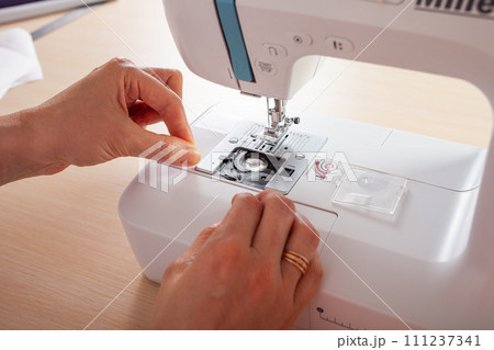 Seamstress at work. Dressmaker making clothes in modern studio. Tailor holding pencil and marking fabric. Woman standing at table with cut textile, sewing machine, thread, pins, needles, tape, cutouts Seamstress at work. Dressmaker making clothes in modern studio. Tailor holding pencil and marking fabric. Woman standing at table with cut textile, sewing machine, thread, pins, needles, tape, cutouts 111237341
