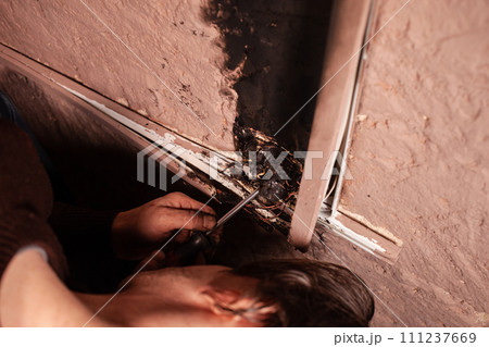 A man fixes a burnt socket. Short circuit, burnt wires. traces of smoke fire on the wall. The electrical outlet was completely melted, the voltage drop from the use of an electric heater. Screwdriver A man fixes a burnt socket. Short circuit, burnt wires. traces of smoke fire on the wall. The electrical outlet was completely melted, the voltage drop from the use of an electric heater. Screwdriver 111237669