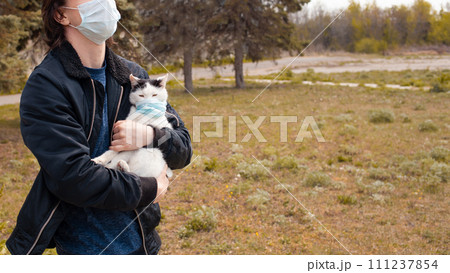 A black and white cat in a medical mask walks on the street 111237854