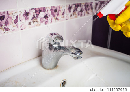 Maid with rubber glove cleaning tap and sink. 111237956