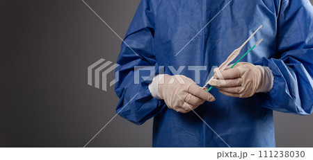 A gynecologist with a venus mirror in his hands. Gynecological accessories, brush, stick. A doctor in a medical mask, a robe, gloves, with a gynecological mirror on a gray background. 111238030