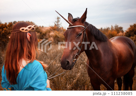 Beautiful young female elf with long dark wavy hair petting her horse resting in the woods forest nymph stroking her horse care pet love animals harmony caring owner gentle creature myth 111238085