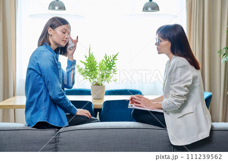 Sad young woman in meeting with psychologist, sitting on couch in office 111239562