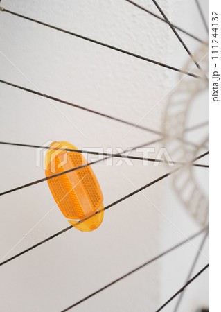 Abstract View of a Yellow Bicycle Reflector Between Spokes Against a White Wall 111244132