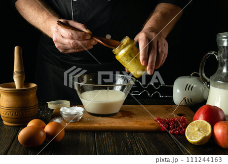 The chef adds honey to a milk dish on the kitchen table. Concept of preparing delicious dinner from eggs and milk in the kitchen The chef adds honey to a milk dish on the kitchen table. Concept of preparing delicious dinner from eggs and milk in the kitchen 111244163