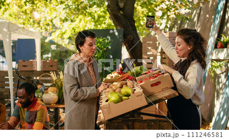 Two men drinking homemade wine and women taking photos, diverse people enjoying autumn day at local farmers market street stand. Cheerful clients and vendors sampling bio products. 111246581