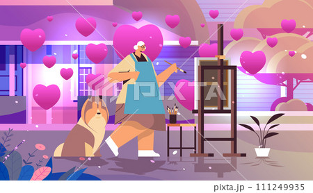 senior woman artist with dog painting picture on backyard with pink love hearts valentines day celebration concept horizontal 111249935