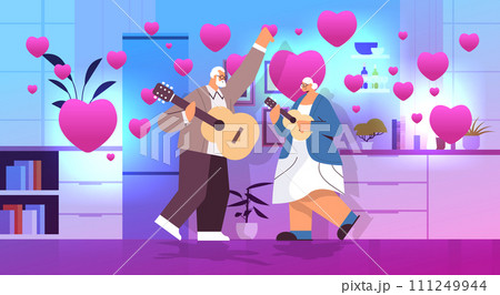 senior couple playing guitar grandparents having fun active old age concept home kitchen interior with pink love hearts valentines day celebration 111249944