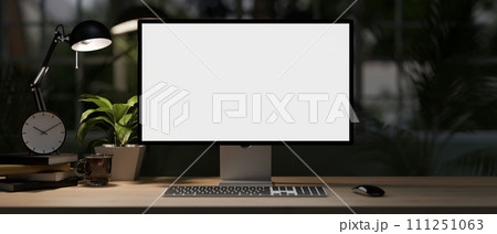 A modern home office desk at night with a white-screen computer mockup, dim light from a table lamp. 111251063