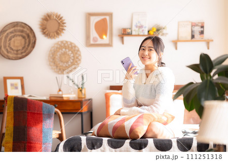 ベットでくつろいでスマホを見る大学生の女性 111251318