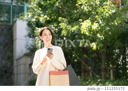 スマホを持つ買い物帰りの女性 111255172