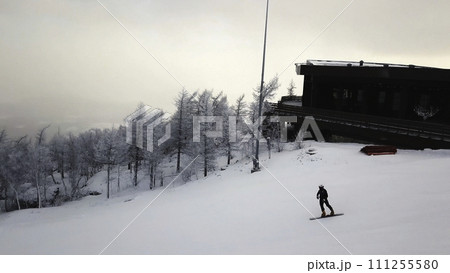 Man sliding on a snowboard, moving down the hill. Stock footage. Aerial view of landscape of ski and snowboard slopes along bald winter trees and a snowboarding man. Man sliding on a snowboard, moving down the hill. Stock footage. Aerial view of landscape of ski and snowboard slopes along bald winter trees and a snowboarding man. 111255580