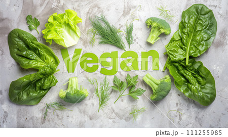 Word Vegan, title text lined up into word from green vegetables on gray table with lettuce, spinach broccoli, parsley, dill 111255985