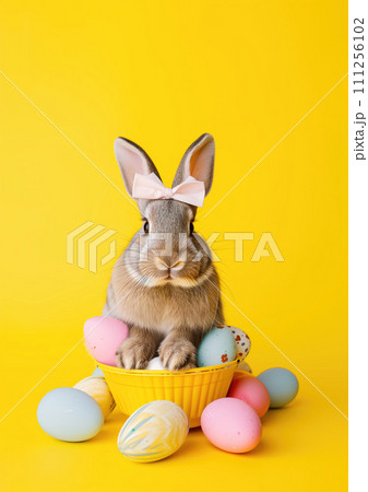 Holiday easter rabbit with bow sitting on colored decorated easter eggs on neutral yellow background 111256102