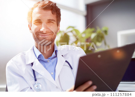 A male doctor in a white coat looks at the medical history and laughs. 111257884