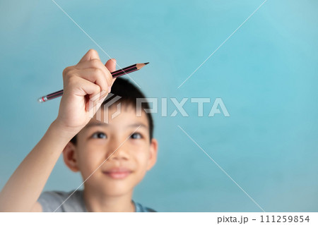 Asian boy holding a pencil drawing in the air, imagination concept of a child on a blue background Asian boy holding a pencil drawing in the air, imagination concept of a child on a blue background 111259854