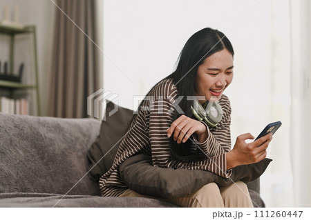 Beautiful young woman relaxing on sofa watching social media on her mobile phone Beautiful young woman relaxing on sofa watching social media on her mobile phone 111260447