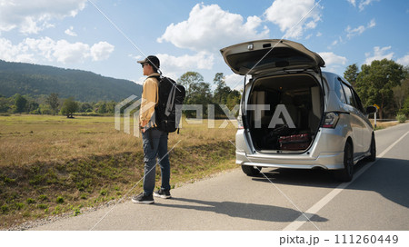 Man carrying backpack standing on countryside and looking at beautiful mountain view. Local solo travel on weekends concept Man carrying backpack standing on countryside and looking at beautiful mountain view. Local solo travel on weekends concept 111260449