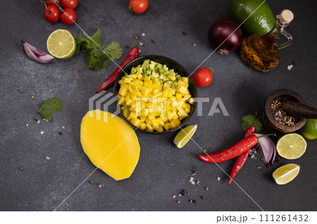 Cooking mango salsa - sliced chopped ingredients in a black ceramic bowl 111261432
